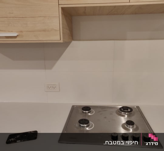 חיפוי קיר קרמיקה לבן במטבח מתחת לארונות עץ וכיריים